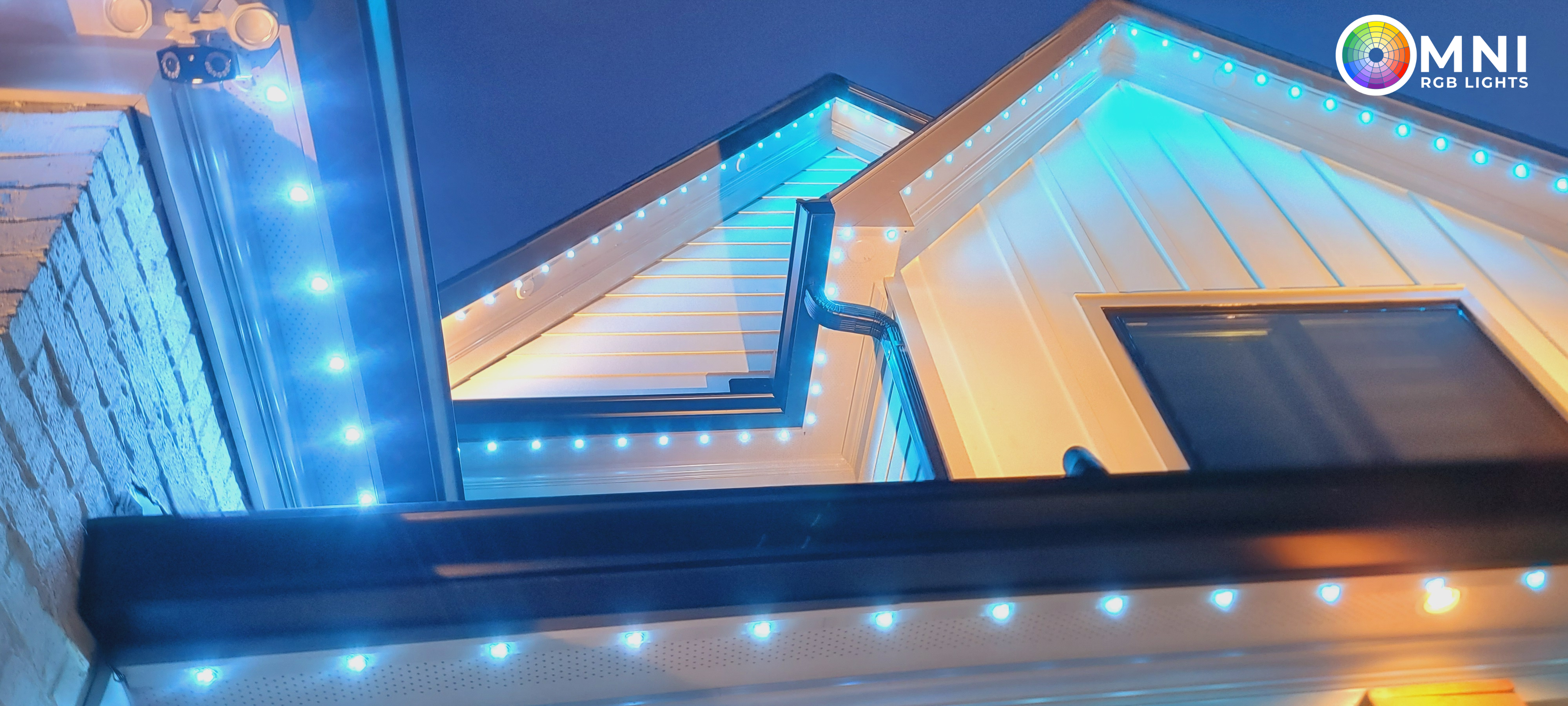 Night view of roofline RGB lighting in cyan along white siding.